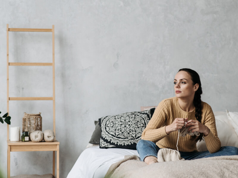 Woman sitting on her bed to unwind whilst crocheting at home. 