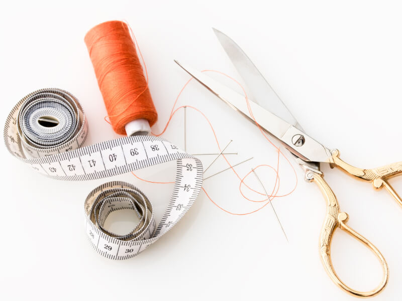 Dressmaking scissors with gold handles lying on a table next to some orange cotton and a rolled up tape measure