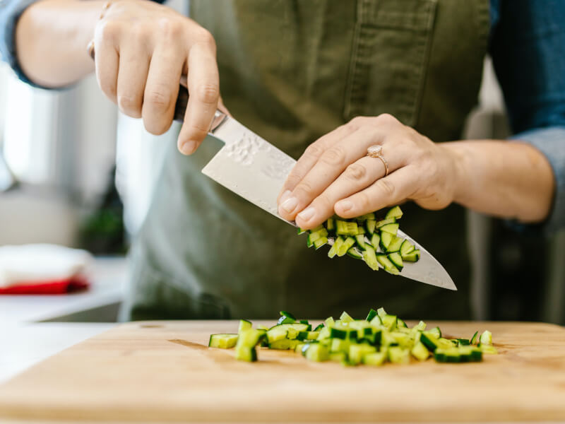 Person slicing cucumber at vegan cooking class.