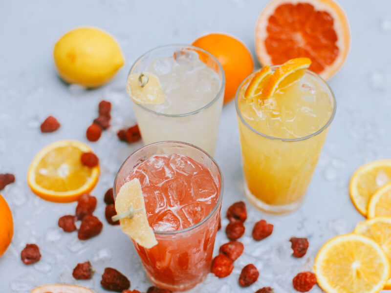 Three summer cocktails spread out with fruit.