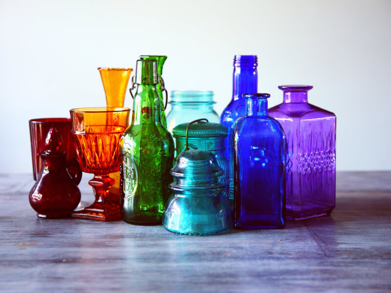 A variety of different coloured glass bottles and containers sit on a table