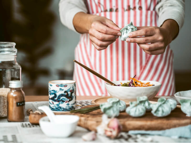 A person wearing a red striped apron is making vegan Asian dumplings