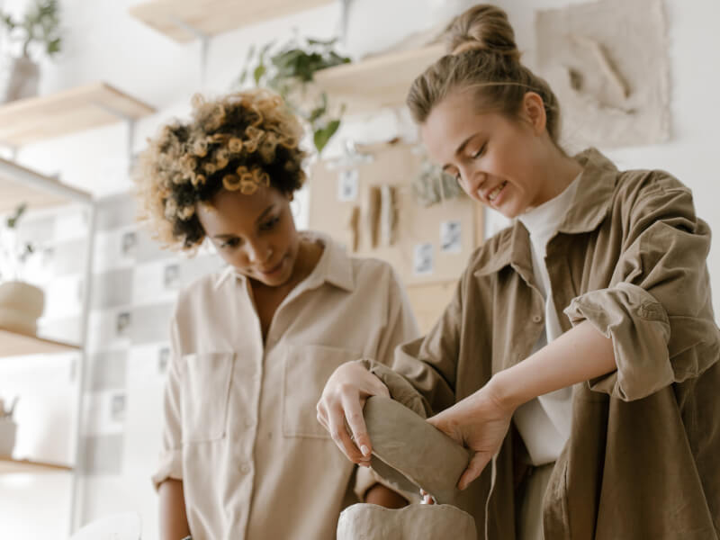 Two friends working together in a pottery studio to build their handmade pottery skills.
