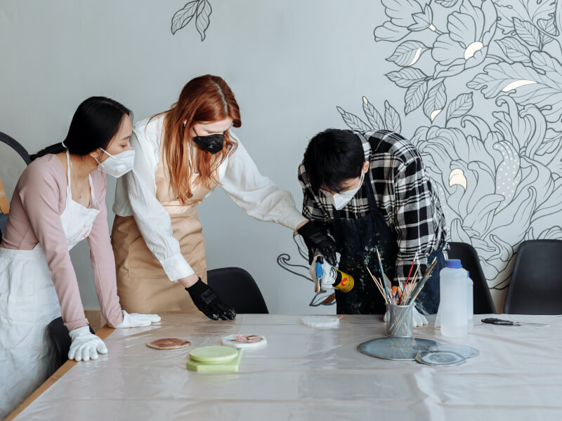 Three people wearing masks pouring resin at a vegan craft class.