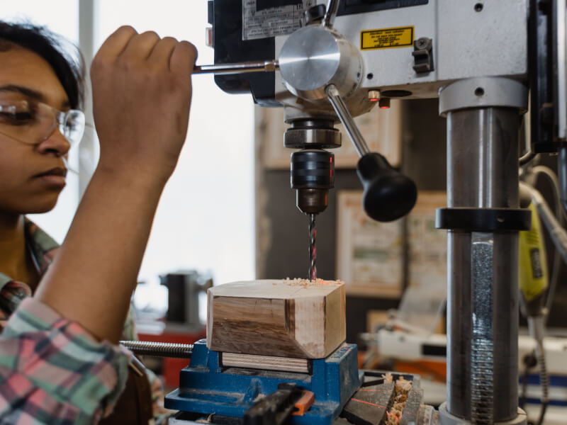 A woman uses a mechanical tool in a woodworking class.