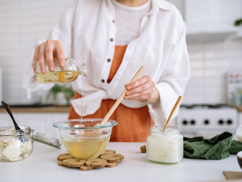 A woman wearing an orange apron is standing at a white table, making candles