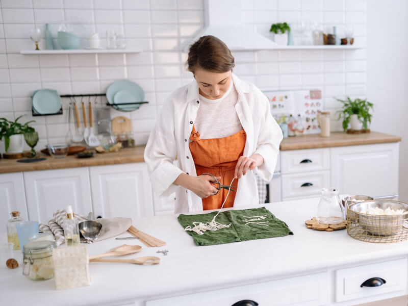 A person is in a kitchen wearing an orange apron, with candle making equipment on the table in front of them