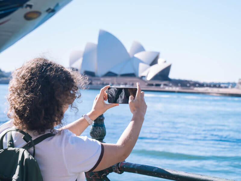 A woman is taking a photo of a building across the water at a photography class