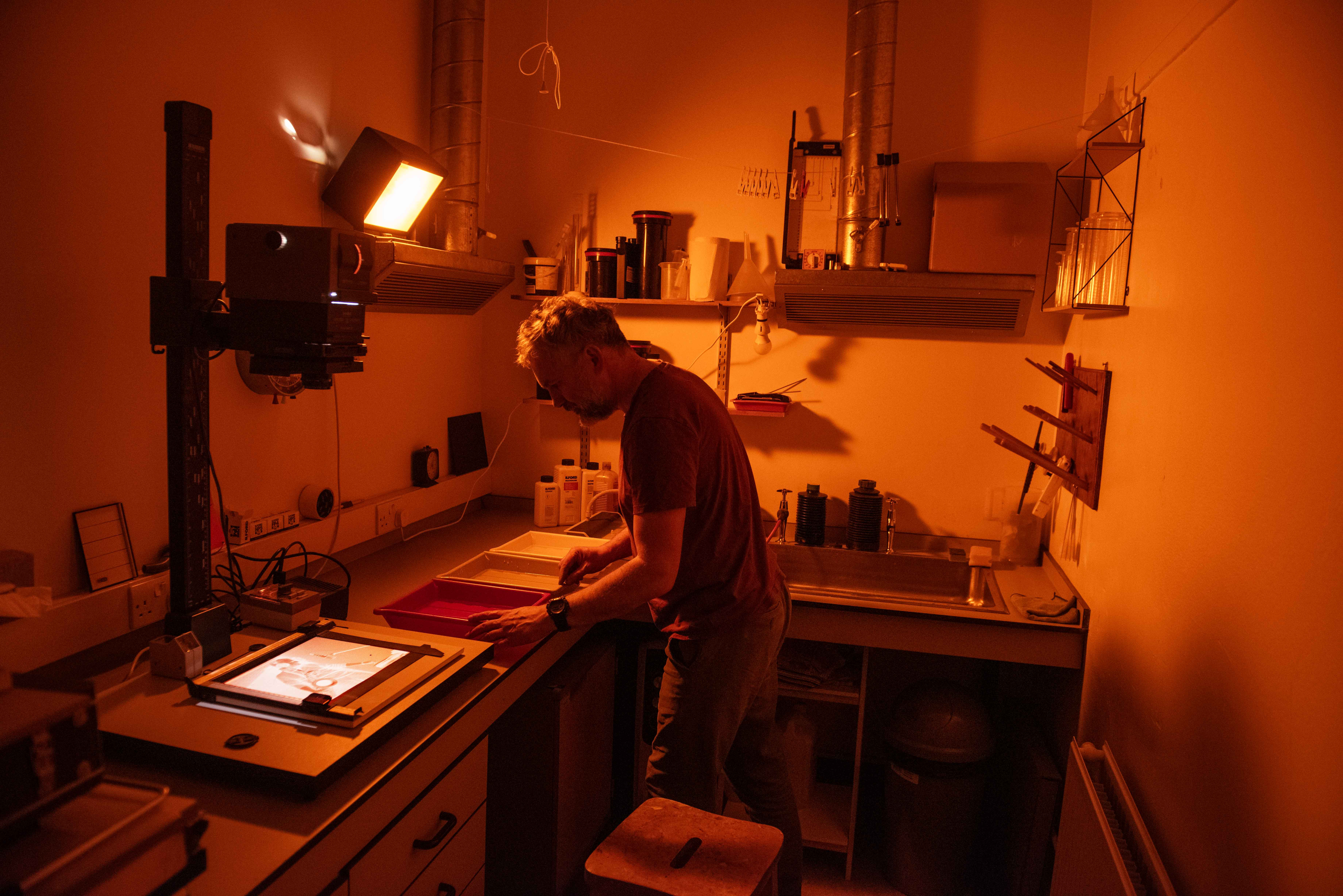 A man in a darkroom surrounded by photography developing equipment