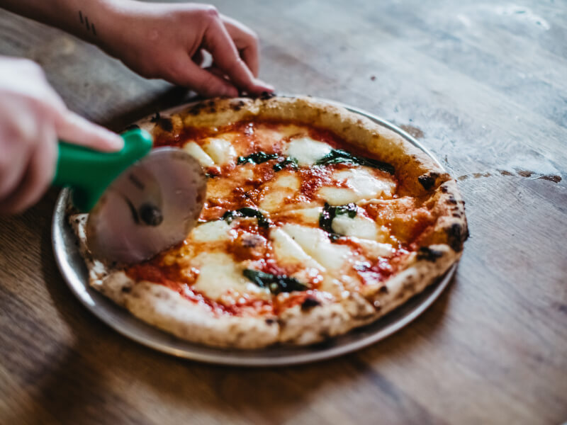 A close up of a person using a pizza wheel to cut a handmade pizza