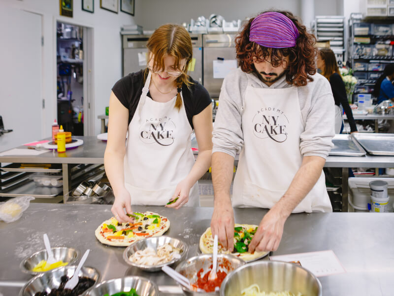 Man and woman adding toppings to a pizza in a cooking class