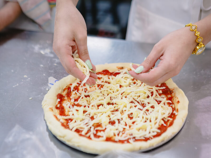 Someone adding cheese to a pizza in a cooking class