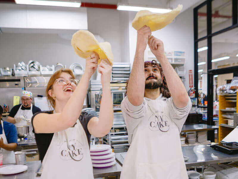 A man and woman spinning dough in a pizza class