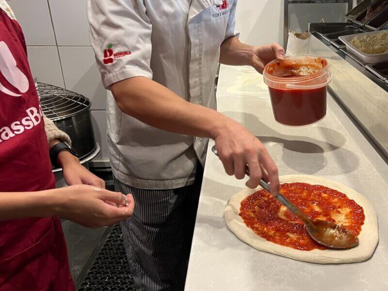Someone adding sauce to a pizza in a cooking class