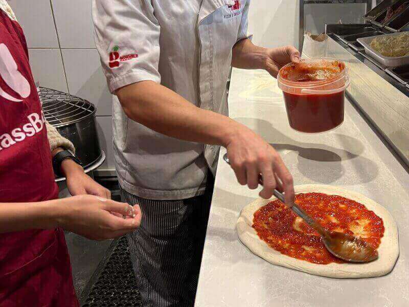Someone spreading tomato sauce on pizza dough.