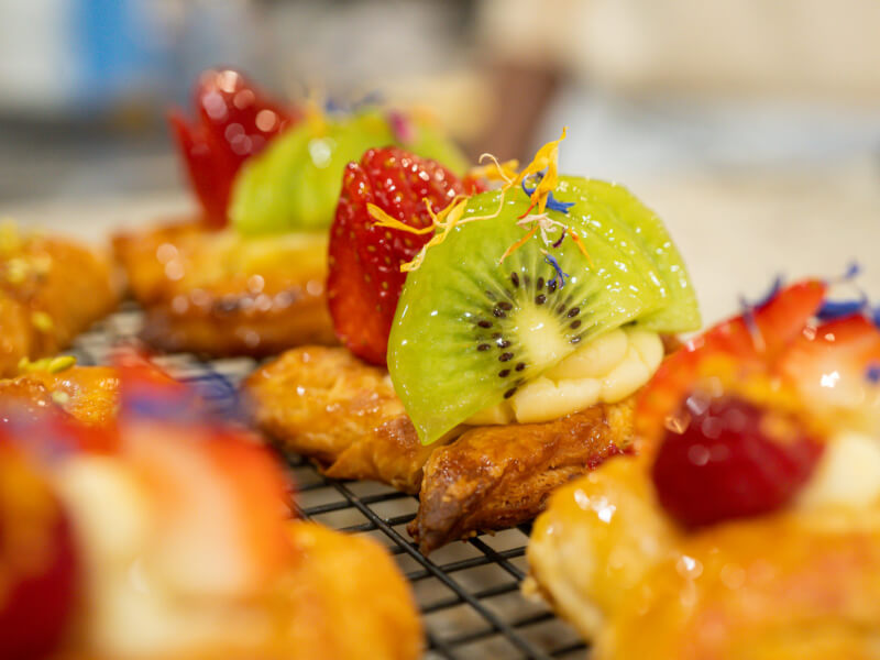 A handmade pastry topped with glazed fruit sits on a cooling tray