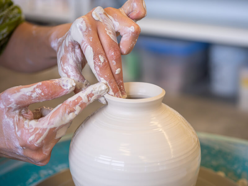 A close up of a person making a small vase on a pottery wheel