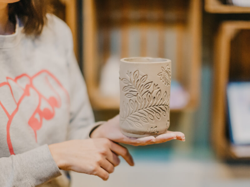 A close up of a person holding a hand built clay pot engraved with flowers and leaves