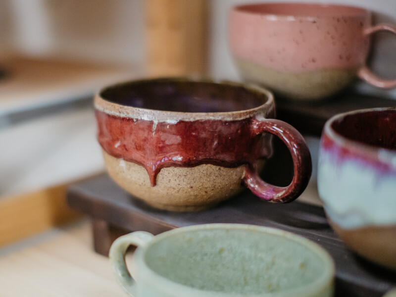 Some handmade ceramic cups finished with colour glaze stand on a shelf