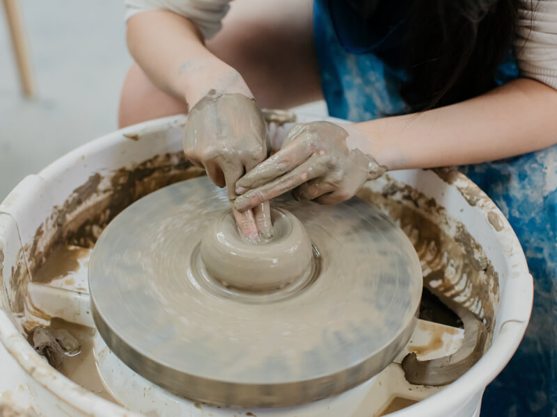 A close up of a person beginning to make a pot or bowl from clay on a pottery wheel