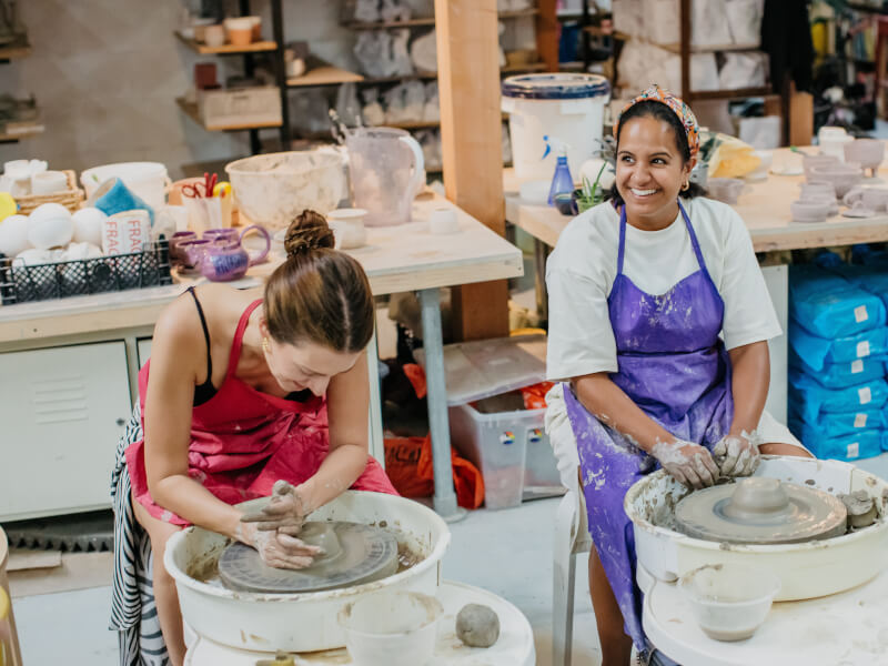 Two women are making clay pots on pottery wheels