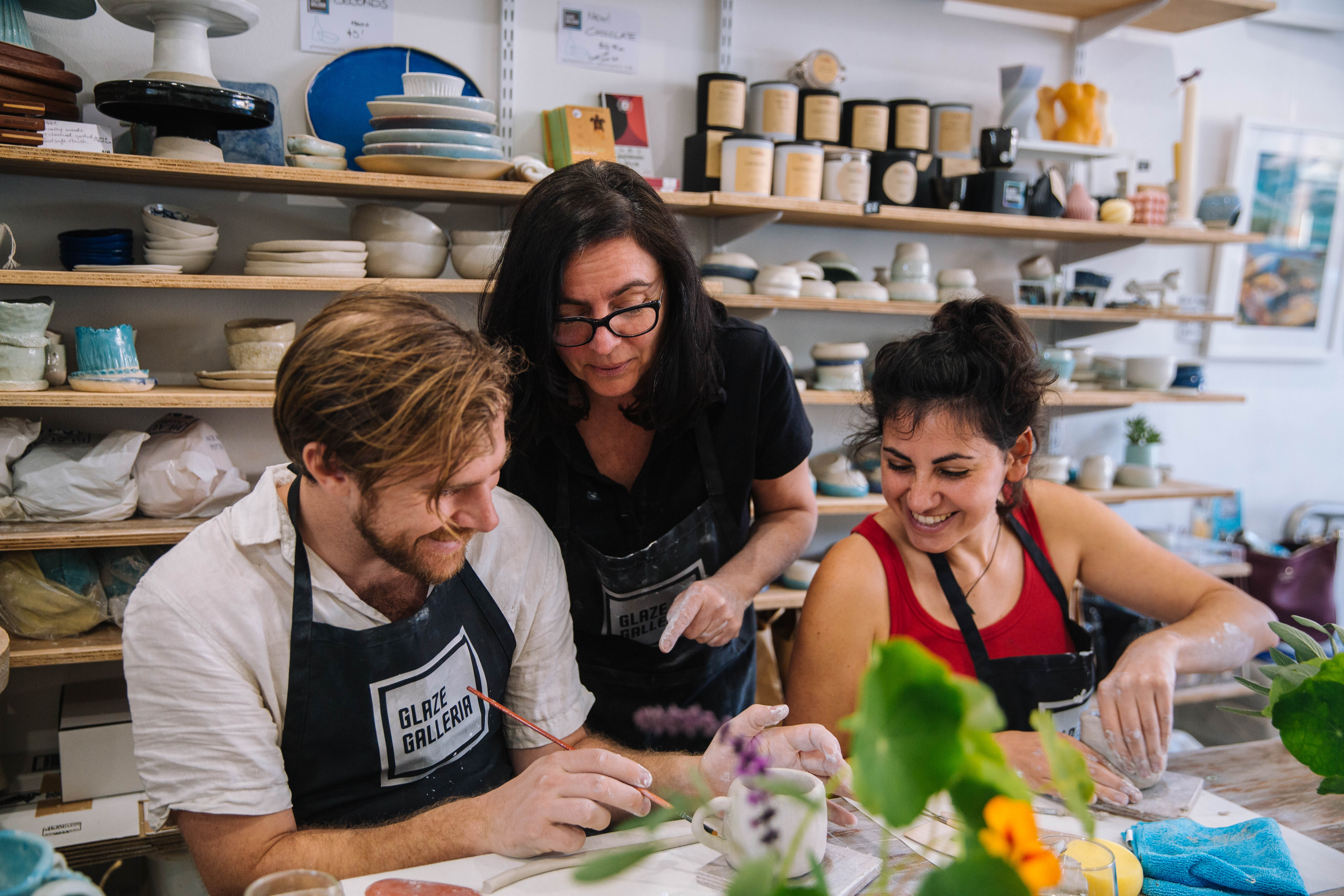 A man and woman sit at a handbuilding pottery class, learning how to make cups from clay