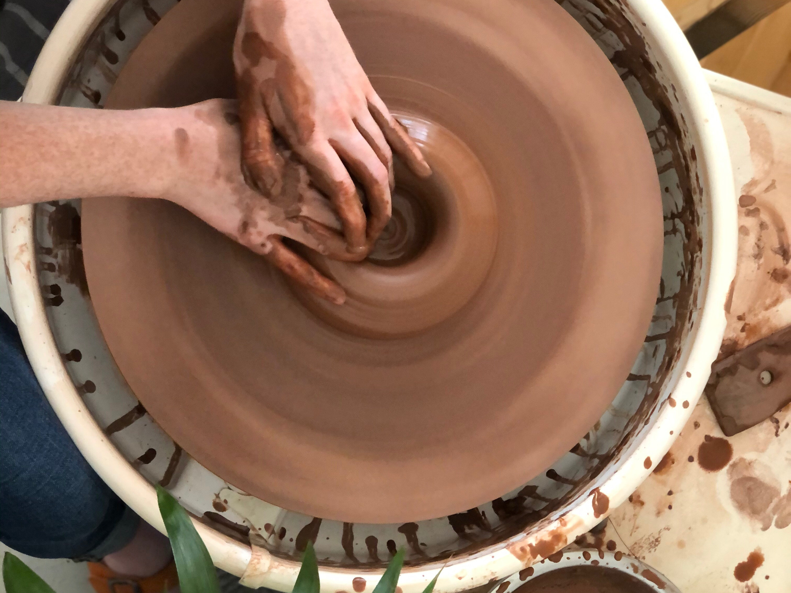 Overhead view of hands working clay on a pottery wheel