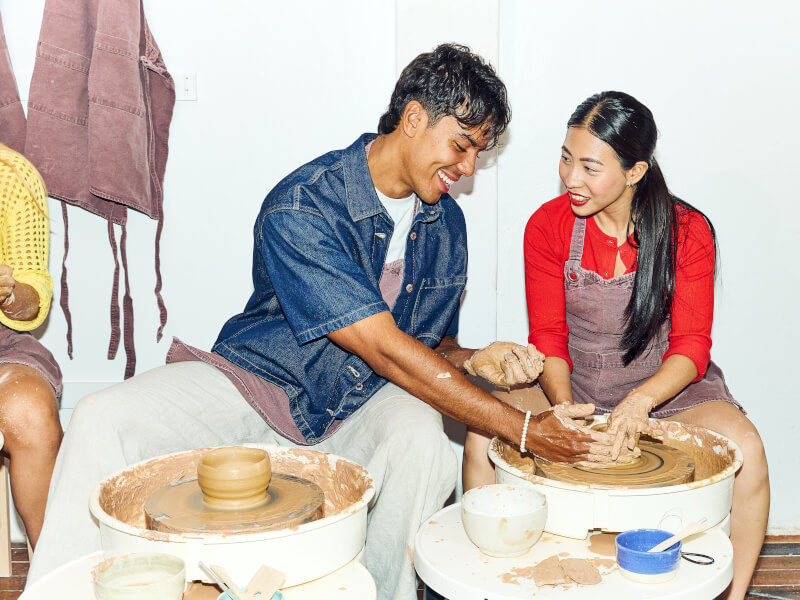 Smiling man and woman working with clay on a pottery wheel