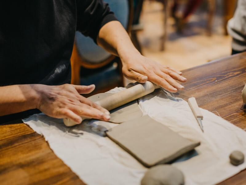 Hands with a rolling pin working with clay in a pottery class