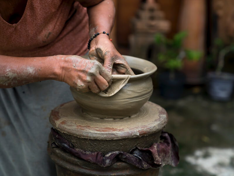 Clay splattered hands shaping a homemade clay bowl with a cloth.  