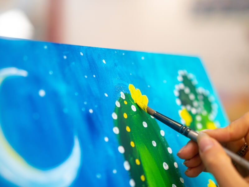 A close up of a person painting a colourful picture in green and blue