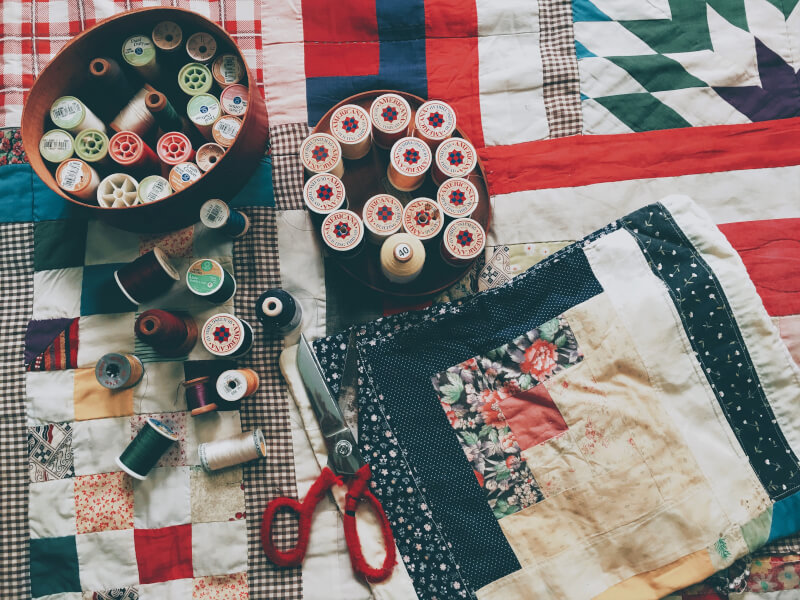 A sewing kit full of supplies lies on a handmade quilt.