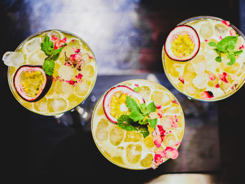 Three passionfruit martinis with lots of ice, mint and rose petals for garnish.