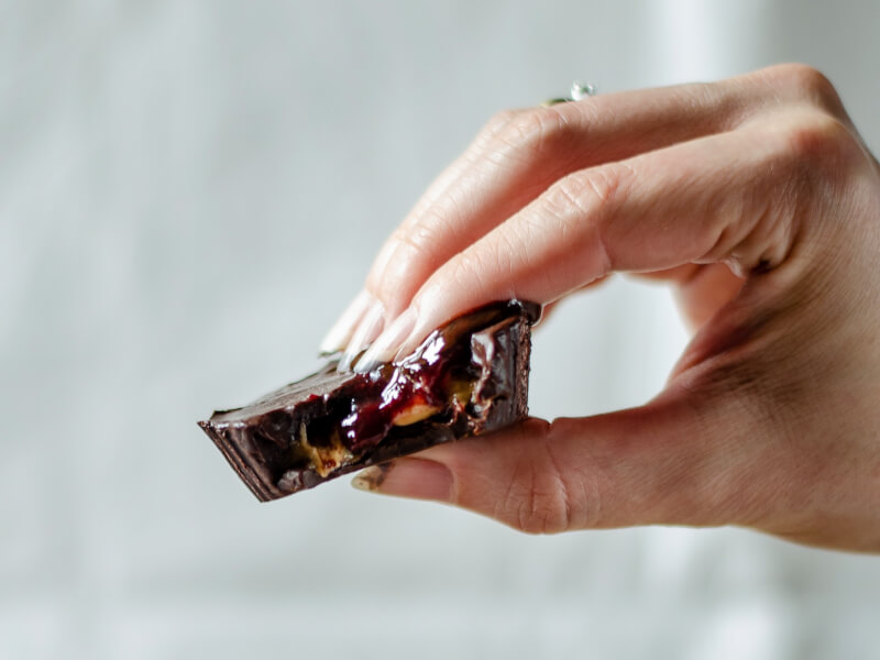 A hand is holding a handmade chocolate with a bite out of it. It has nuts and jam in the centre.