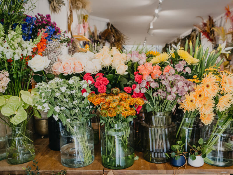 A room full of brightly coloured flowers in different styles of vases 