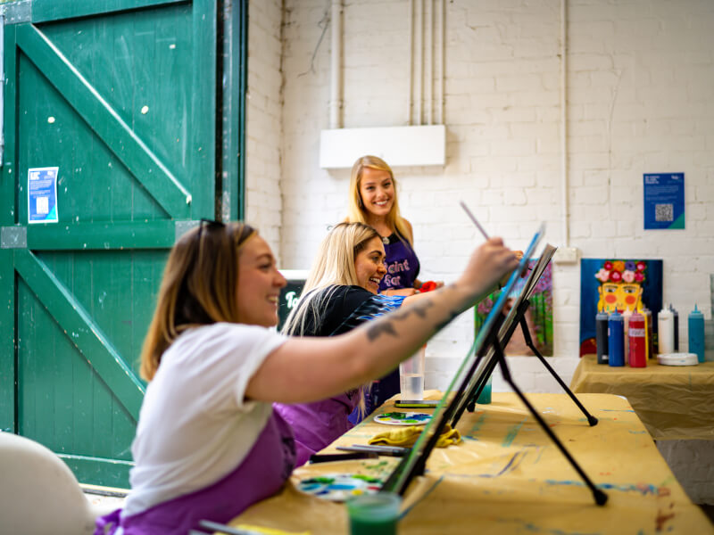 Two women are sitting at easels painting, at an art class in Glasgow