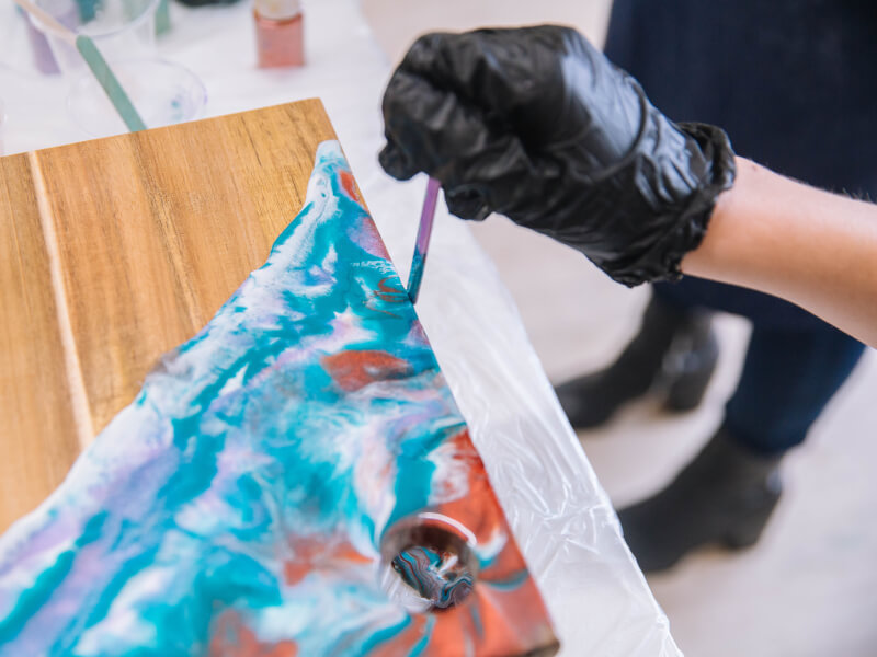 A close up of a person decorating a chopping board using the fluid art technique at an art workshop in Glasgow