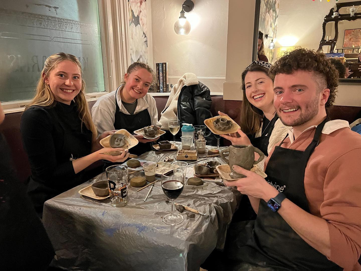 A group of people at a table are smiling and holding handmade pottery projects