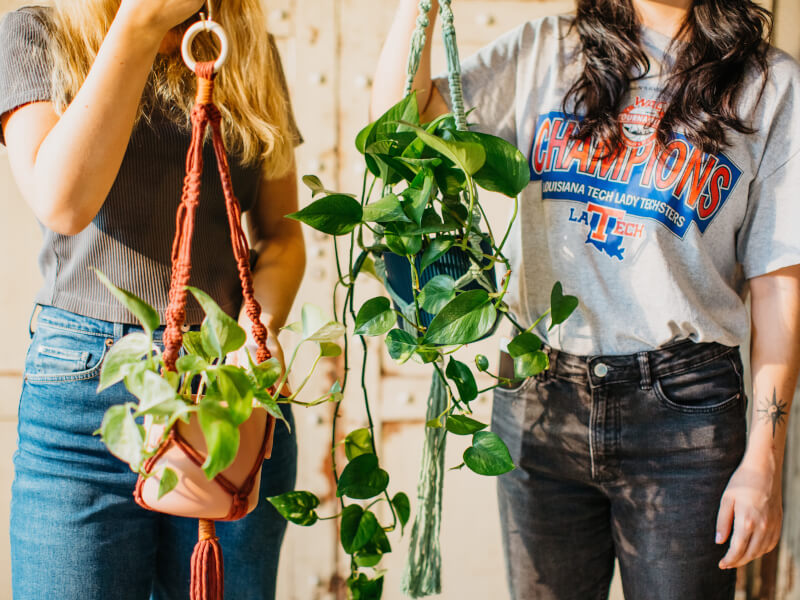 Two people are holding two handmade macrame planters in green and orange