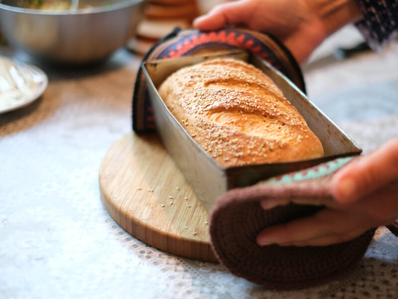 A freshly baked loaf of bread sits in a tin on a breadboard