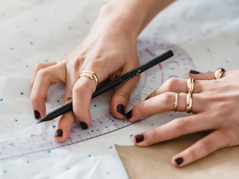 A close up of a person's hands using a ruler to measure and draw a paper sewing pattern