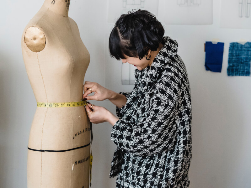 A person is measuring the waist of a tailor's dummy