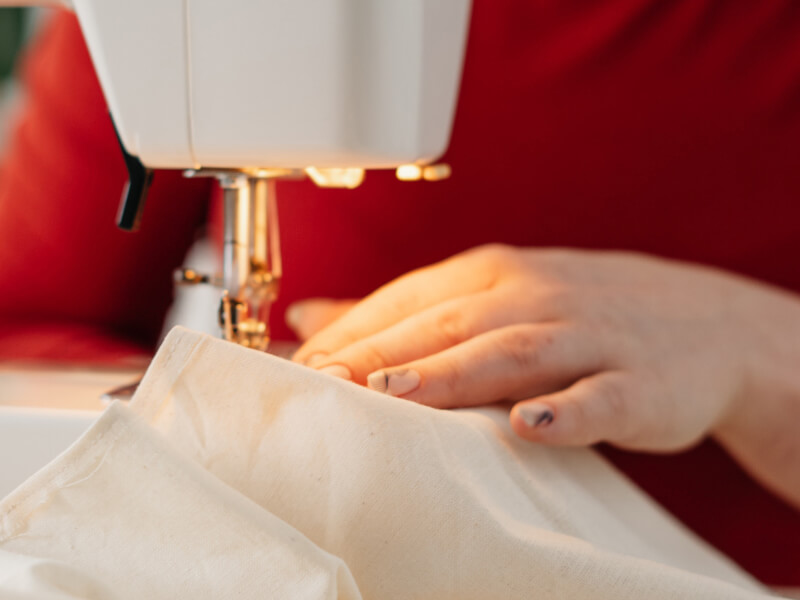 A close up of a person sewing beige fabric on a sewing machine