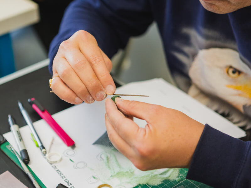 A close up of a person filing a mould during a silver jewellery making class.