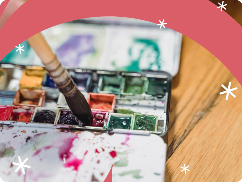 A paintbrush being dipped into a paint palette.