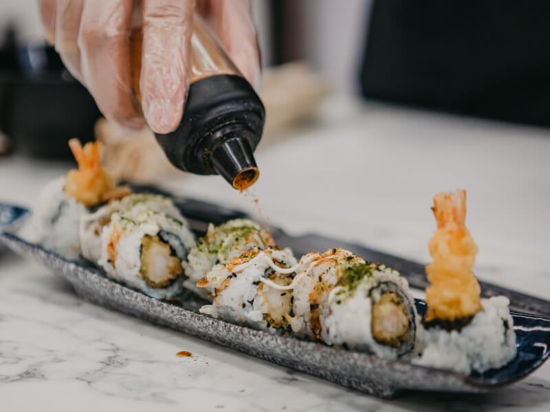 A close up of someone adding sauce to a plate of handmade sushi