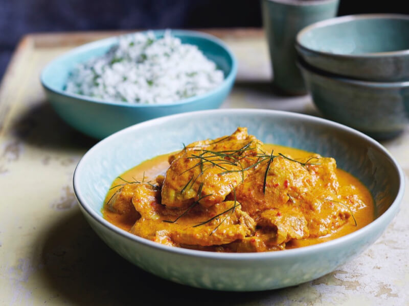 A spicy Asian dish sits in front of a bowl of rice, in blue bowls on a table