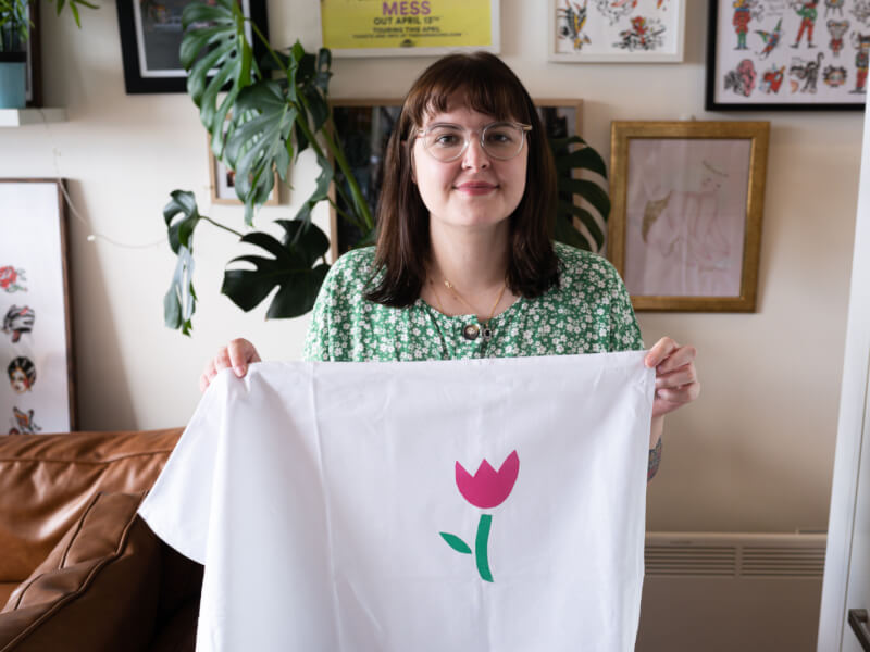A person holding up a piece of white cloth with a pink and green screen printed flower 