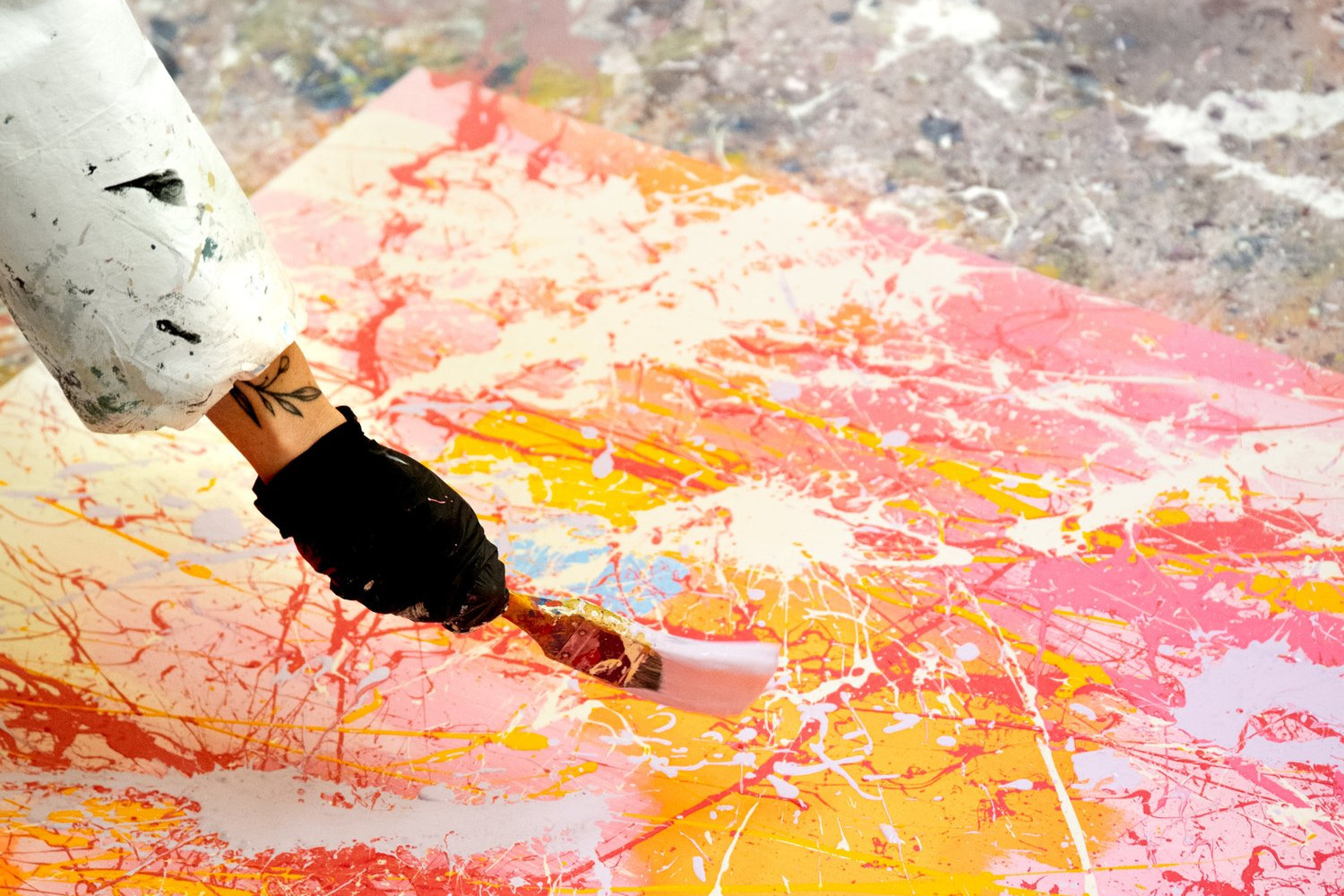 Close up of a hand with a paintbrush applying colourful paint to a canvas