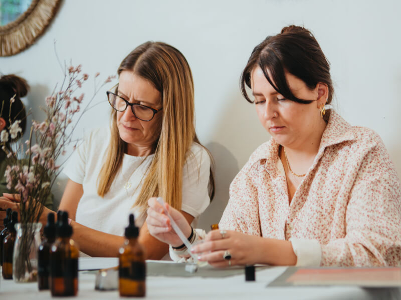 Two women sit at a table, blending essential oils to make perfume